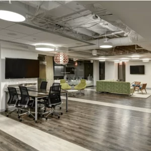 Modern office interior featuring luxury vinyl tile flooring, collaborative workspace with a table and ergonomic chairs, vibrant green lounge seating, and contemporary lighting fixtures.