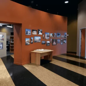 Interior view of a room featuring a table and a wall displaying photographs, with contrasting vinyl composite tile flooring in a modern design.