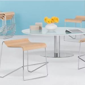 Wake Cafe Lunchroom Chair Stool 3 in a modern cafe setting, featuring sleek design with wooden seat and chrome legs, arranged around a circular glass table with decorative flowers and a tablet.