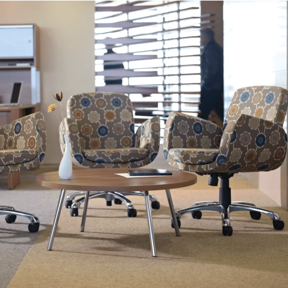 Kate Guest and Meeting Chairs in a modern office setting, featuring patterned upholstery, a round wooden table, and a decorative vase with flowers.