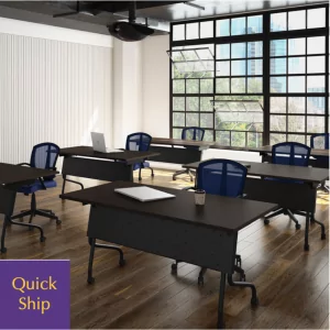 Training tables arranged in a well-lit room with large windows, featuring modern design and blue chairs, labeled "Quick Ship" for fast delivery.