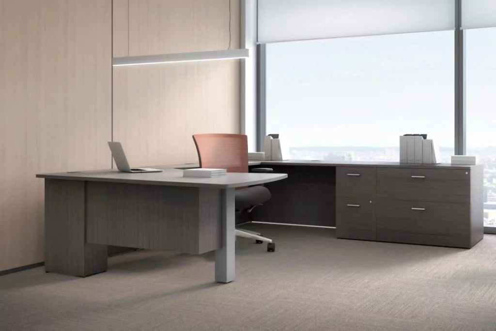 Modern office workspace featuring a wooden desk, ergonomic chair, laptop, and filing cabinets with a city view through large windows.